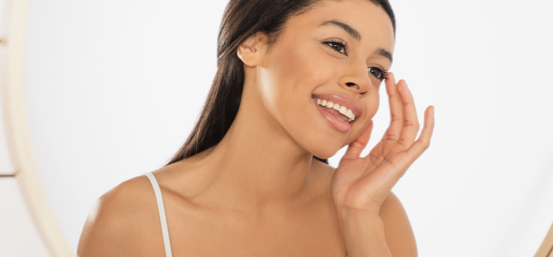 A woman looks joyfully into the mirror, her smile highlighting the radiant skin that may follow glutathione IV drip treatments.