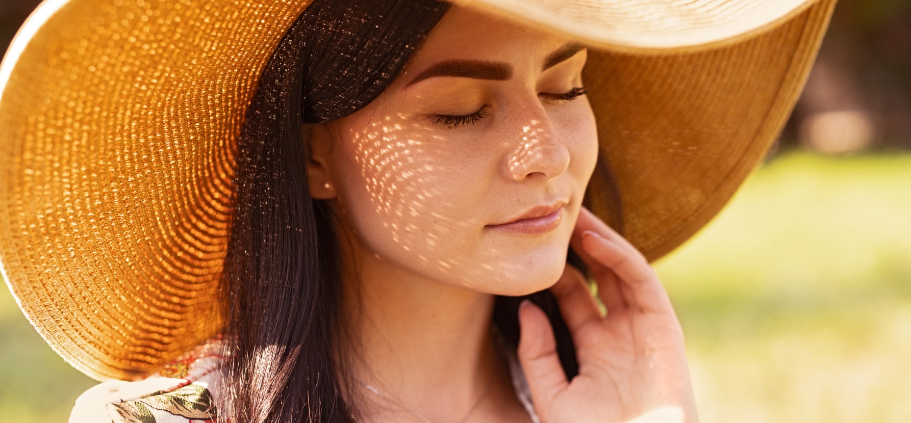 A woman wearing a stylish hat stands in the sunlight, showcasing a blend of fashion and sun protection for her skin.